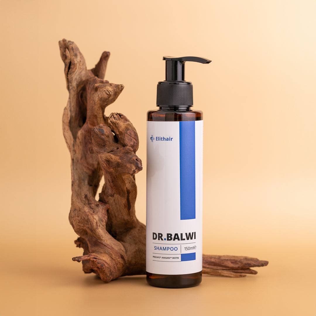 Eine Flasche Dr. Balwi Hair Boost Set Shampoo mit Procapil™ und Pumpspender von shop.elithairtransplant steht aufrecht vor Treibholz auf beigem Hintergrund und zeigt ihr weiß-blaues Etikett.