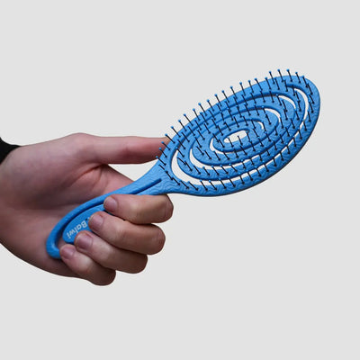 Jemand hält die Dr. Balwi Haarbürste aus dem Dr. Balwi Shop und hebt das elegante Design und die sanften Noppen mit dem einzigartigen spiralförmigen Borstenmuster vor einem schlichten hellgrauen Hintergrund hervor.