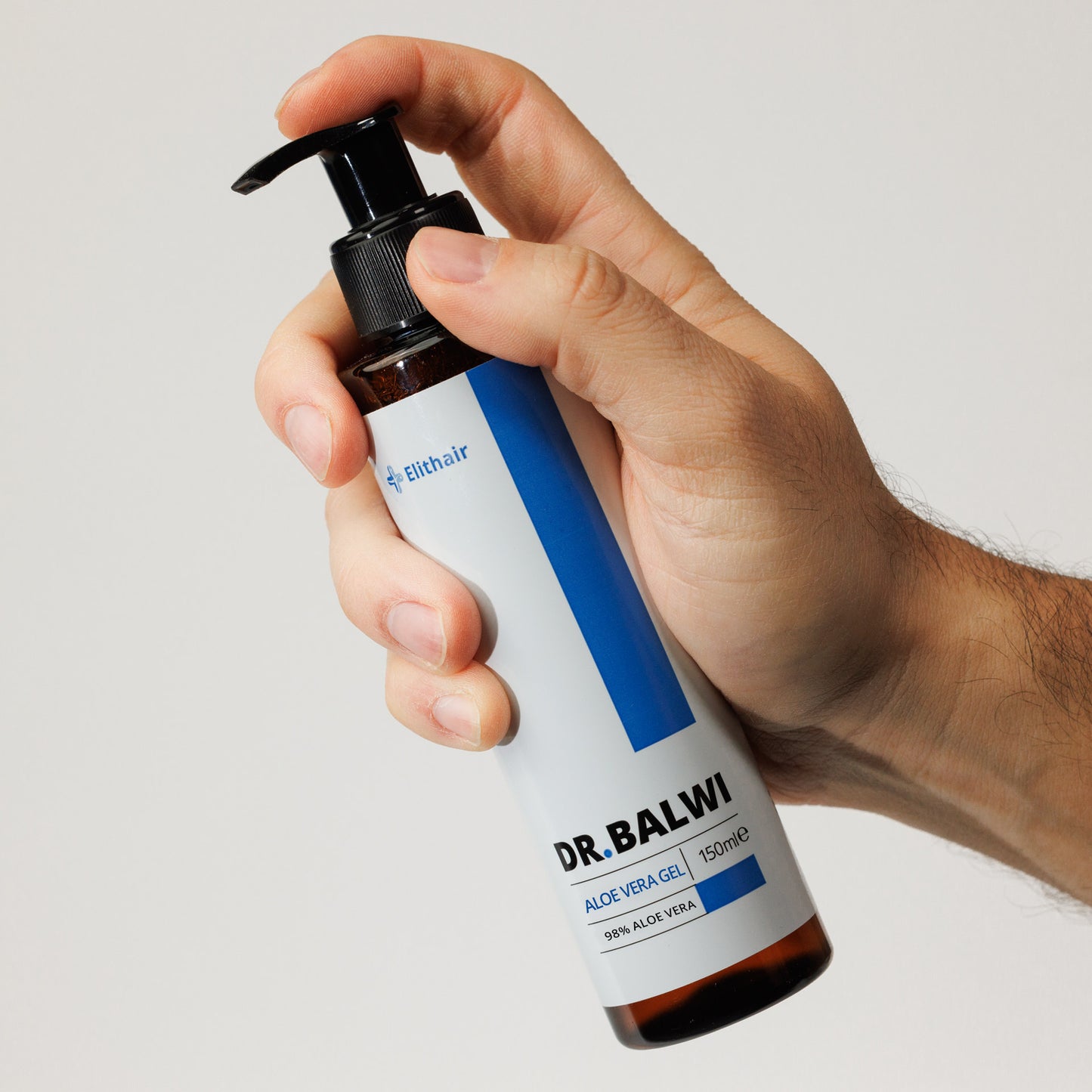 Eine Hand hält eine Flasche Dr. Balwi 98 % Aloe Vera von shop.elithairtransplant mit schwarzer Pumpe und weißem Etikett mit blauen Akzenten. Diese 150-ml-Feuchtigkeitscreme enthält 98 % Aloe Vera für intensive Feuchtigkeitsversorgung.