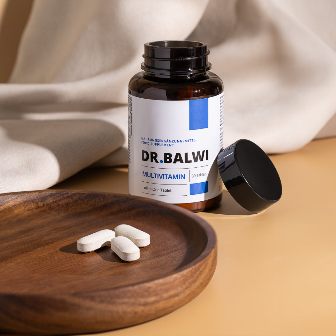 Eine geöffnete Flasche Multivitamin Complex von shop.elithairtransplant steht auf einer beigen Fläche, daneben der schwarze Deckel und vier weiße Tabletten auf einem Holzteller. Im Hintergrund ist cremefarbener Stoff drapiert.