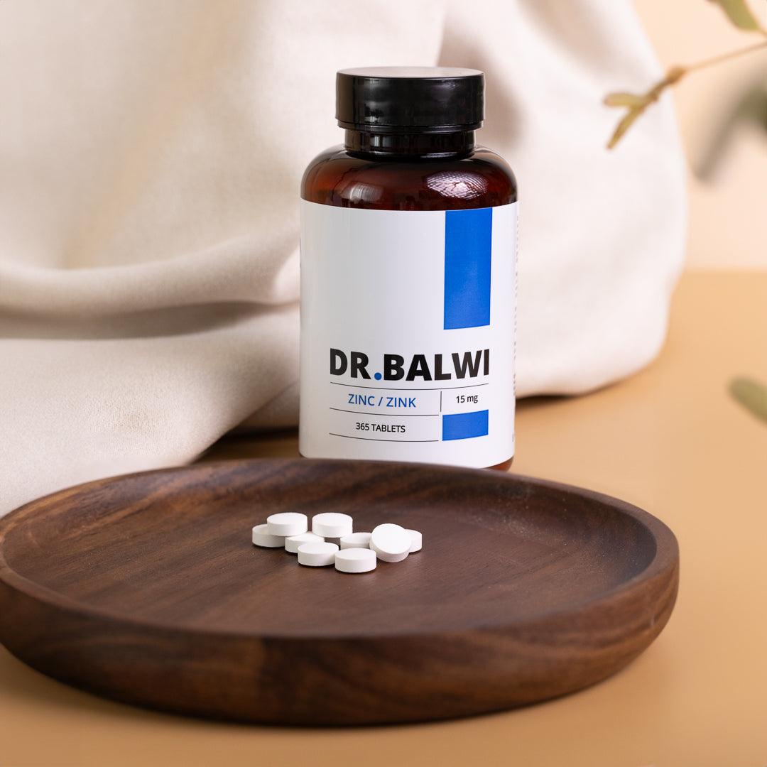 Eine braune Flasche mit der Aufschrift „shop.elithairtransplant Zink Tabletten“ steht auf einer beigen Fläche neben einem Holzteller mit weißen Tabletten zur Unterstützung von Immunsystem und Haarwachstum. Im Hintergrund sind ein cremefarbenes Tuch und Pflanzenblätter zu sehen.