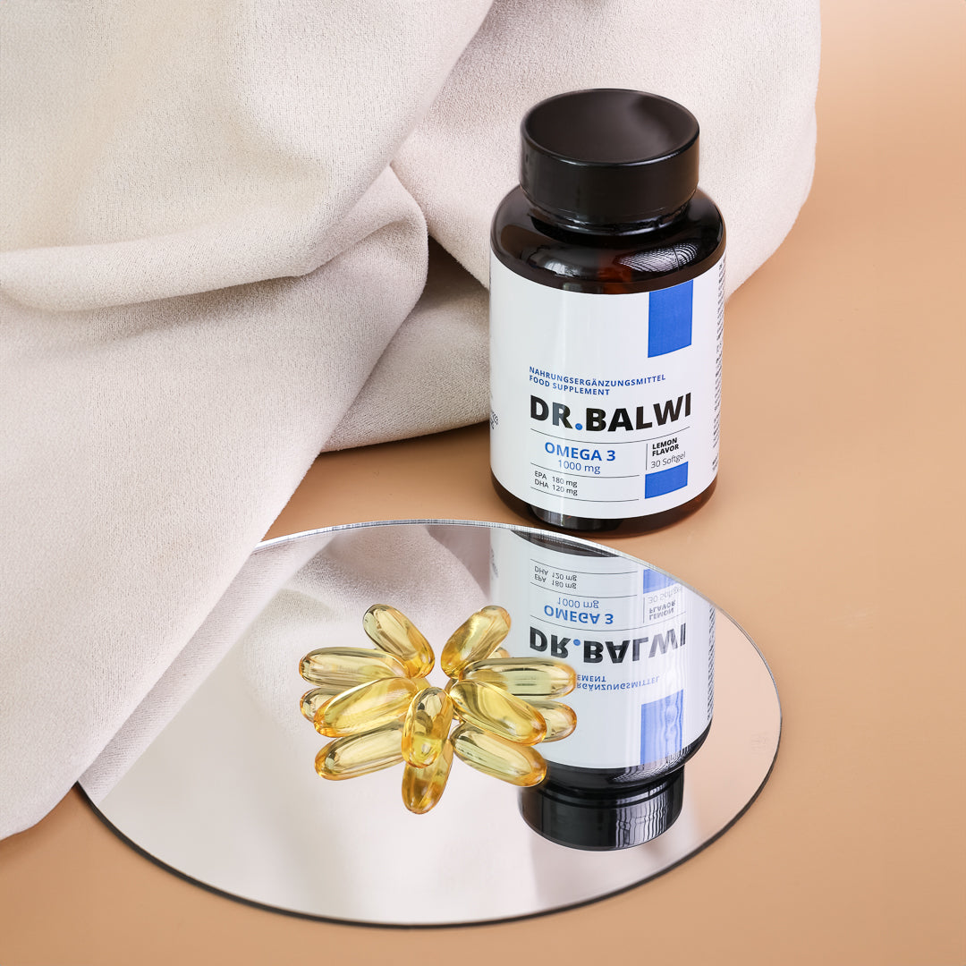 Eine Flasche mit der Aufschrift „shop.elithairtransplant Daily Omega 3“ steht neben einem runden Spiegel, in dem sich gelbe Omega-3-Kapseln spiegeln, die das Haarwachstum fördern. Im Hintergrund ist ein beiges Tuch und eine hellbraune Fläche zu sehen.