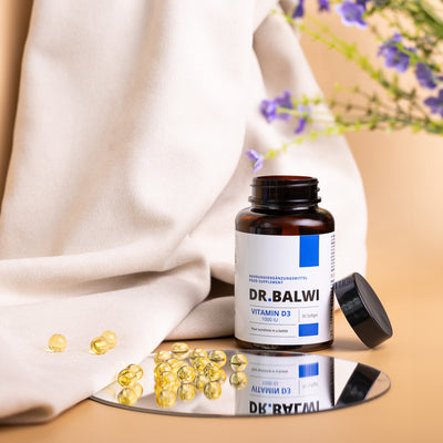 Eine Flasche Vitamin D 1000 IE Softgels von shop.elithairtransplant steht auf einer Spiegelfläche, daneben gelbe Kapseln. Ein beiges Tuch und violette Blumen bilden einen weichen, natürlichen Hintergrund – ideal zur Unterstützung des Vitamin-D- und Immunsystembedarfs.