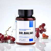 Eine Flasche Biotin- und Keratintabletten von shop.elithairtransplant zur Unterstützung des Haarwachstums ist auf einer weißen Fläche abgebildet. Daneben stehen rote Trauben, ein Becherglas und ein Glas mit klarer Flüssigkeit.