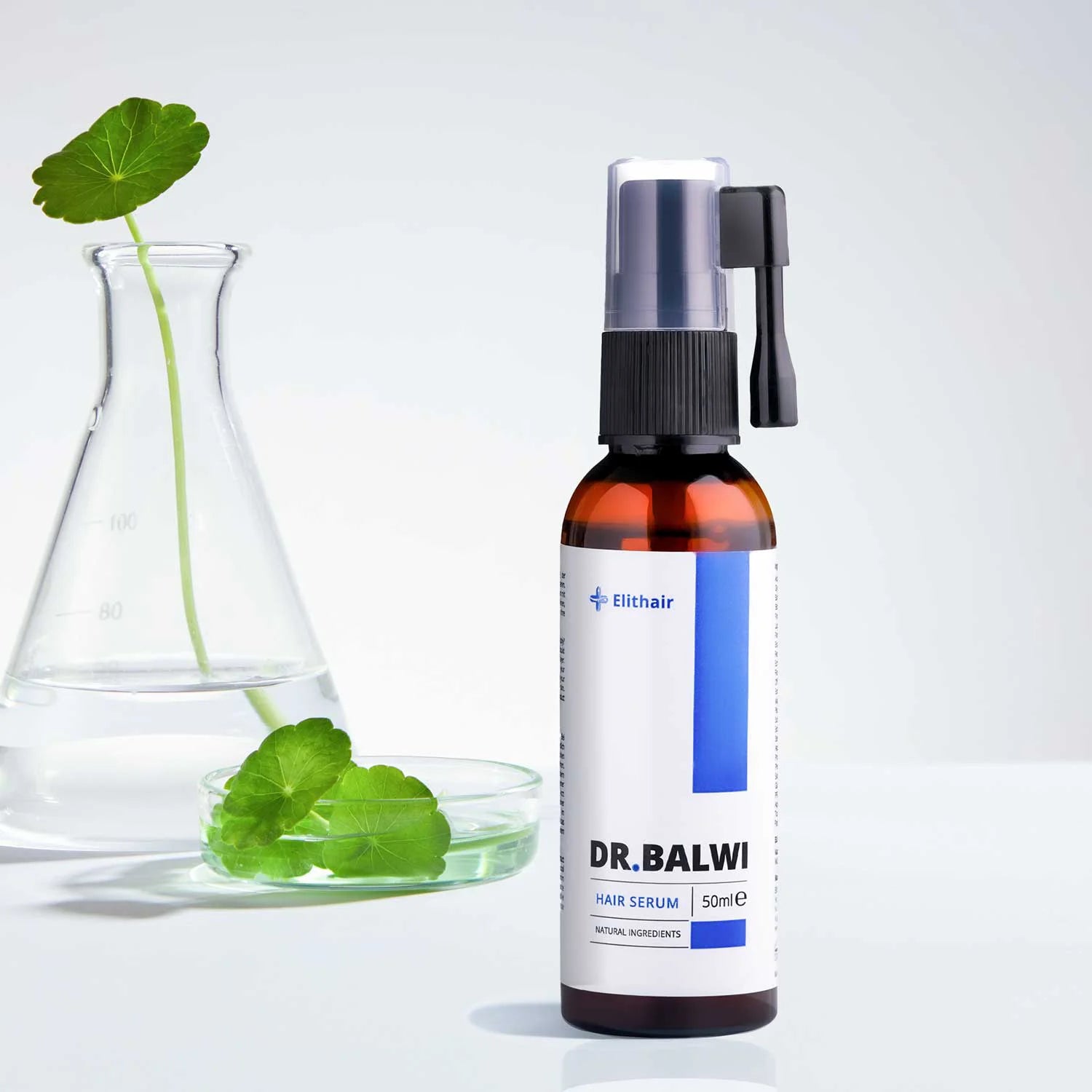 Eine braune Flasche Dr. Balwi Hair Serum von shop.elithairtransplant (50 ml, Sprühverschluss) steht neben einem Becher und einer Petrischale mit grünen Blättern und zeigt auf einer weißen Oberfläche pflanzliche Stammzellen für das Haarwachstum.