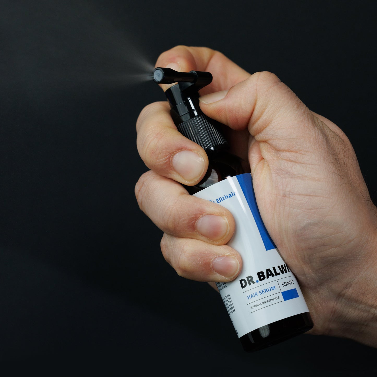Eine Hand sprüht die Shampoo- und Spray-Set-Flasche von shop.elithairtransplant vor einem dunklen Hintergrund und setzt dabei einen sichtbaren Nebel frei – gezielt gegen erblich bedingten Haarausfall.