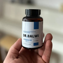 Eine Hand hält eine braune Flasche mit der Aufschrift "Vitamin D 1000 IE" von Dr. Balwi Shop mit einer schwarzen Kappe. Ideal für alle, die sich über Vitamin-D-Mangel oder Haarausfall Sorgen machen. Der Hintergrund ist unscharf.