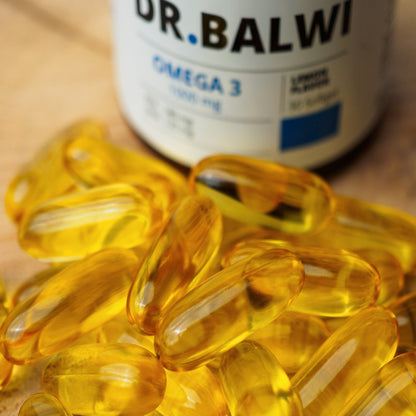 Eine Nahaufnahme mehrerer gelber Daily Omega 3-Kapseln von shop.elithairtransplant, die auf einer Oberfläche verstreut sind, mit einer unscharfen Flasche im Hintergrund – ideal für Haarwachstum und zur Unterstützung gesunder Haare.