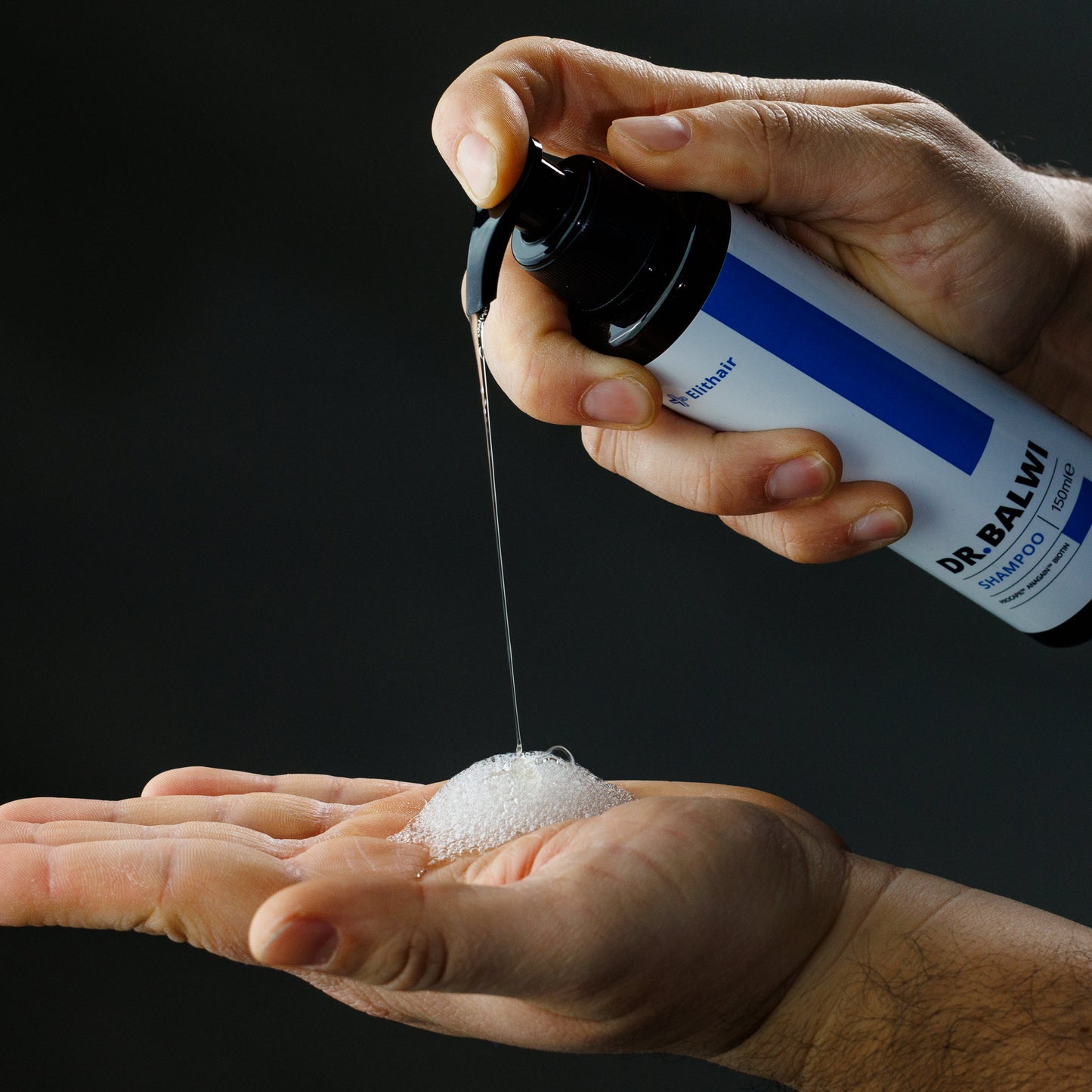 Vor einem dunklen Hintergrund pumpt eine Person schäumendes Shampoo & Spray Set von shop.elithairtransplant aus einer Markenflasche auf ihre offene Handfläche.