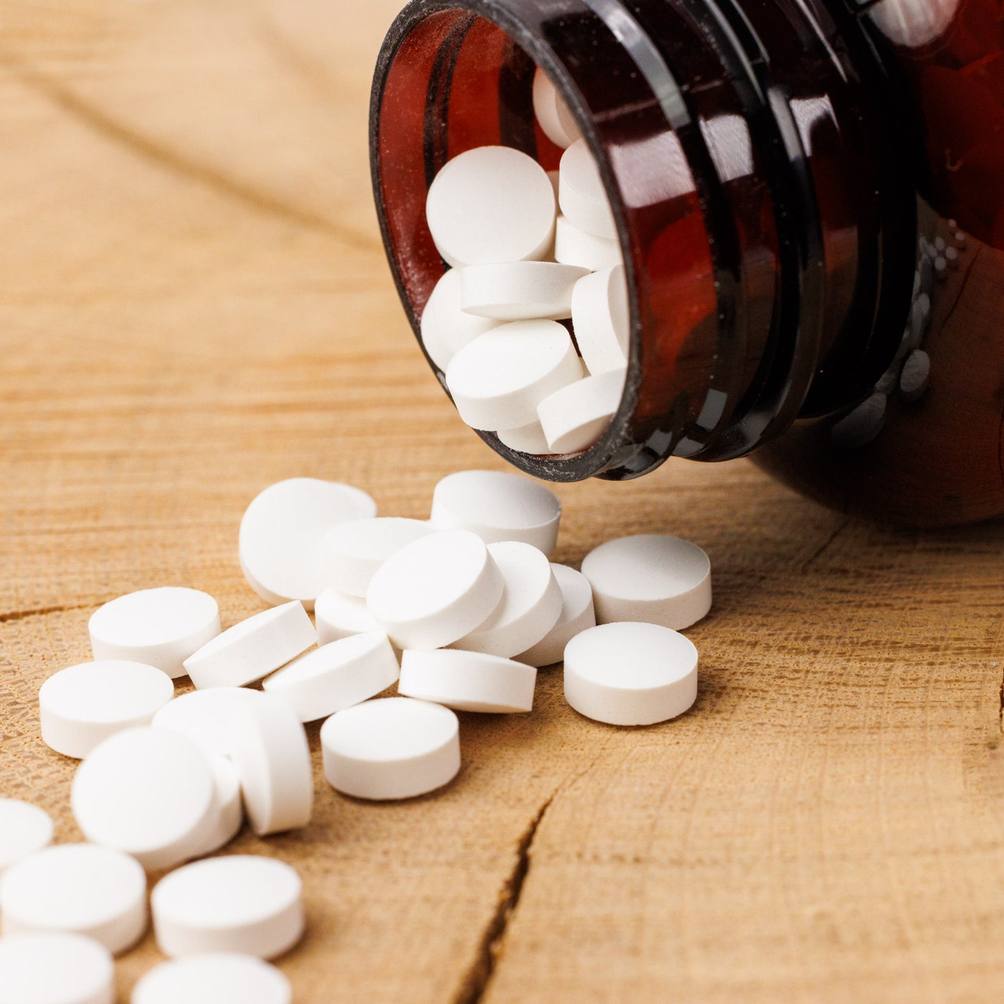 Eine braune Glasflasche von shop.elithairtransplant ist auf Holz umgekippt und hat kleine runde weiße Zinktabletten verschüttet, die das Haarwachstum und ein gesundes Immunsystem unterstützen.